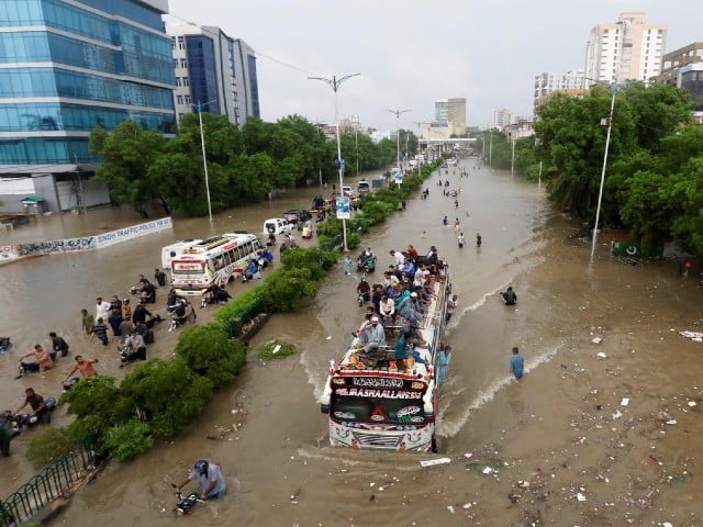 people sit atop a bus roof while others wade through the flooded road during monsoon rain in karachi on august 27 2020 photo reuters