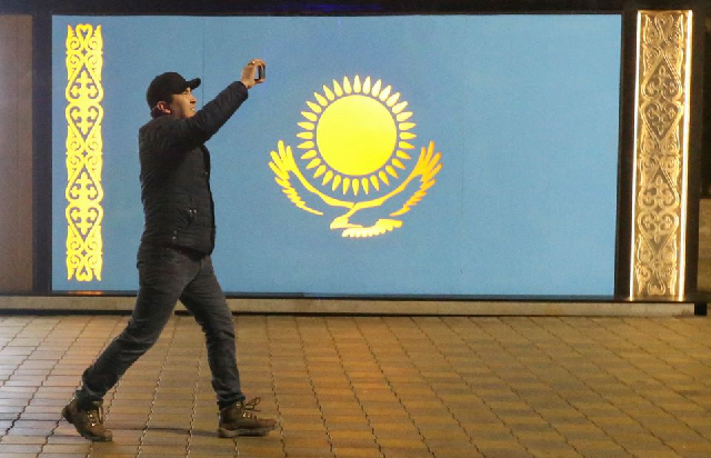 a man holds a mobile phone while walking past a board with a kazakh state flag during a protest against lpg cost rise following authorities decision to lift price caps on liquefied petroleum gas in almaty kazakhstan january 5 2022 photo reuters