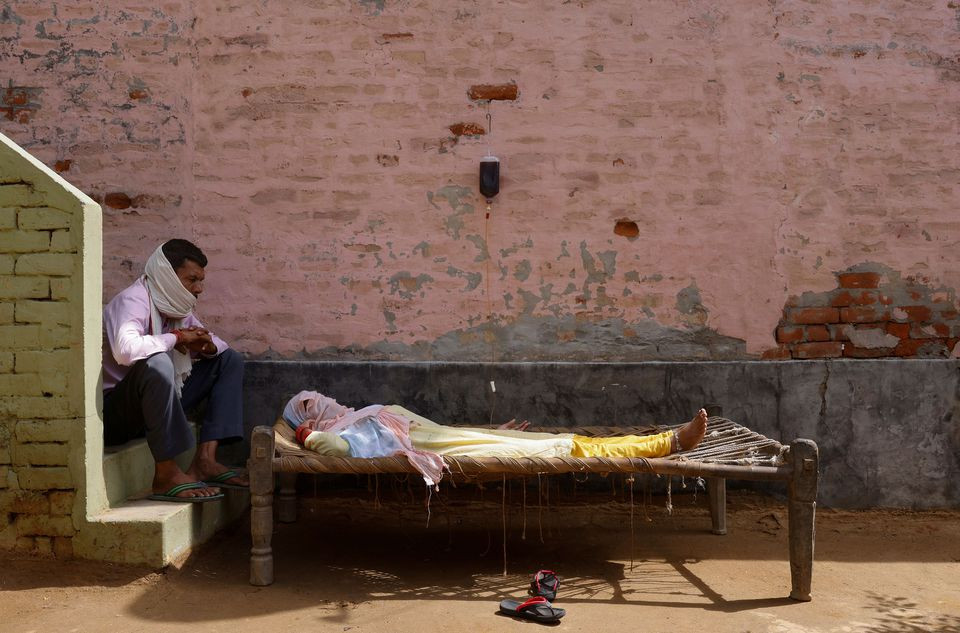 a man sits next to his wife who is suffering from fever as she receives treatment at a clinic set up by a local villager amidst the spread of the coronavirus disease covid 19 in parsaul village in greater noida in the northern state of uttar pradesh india may 22 2021 photo reuters