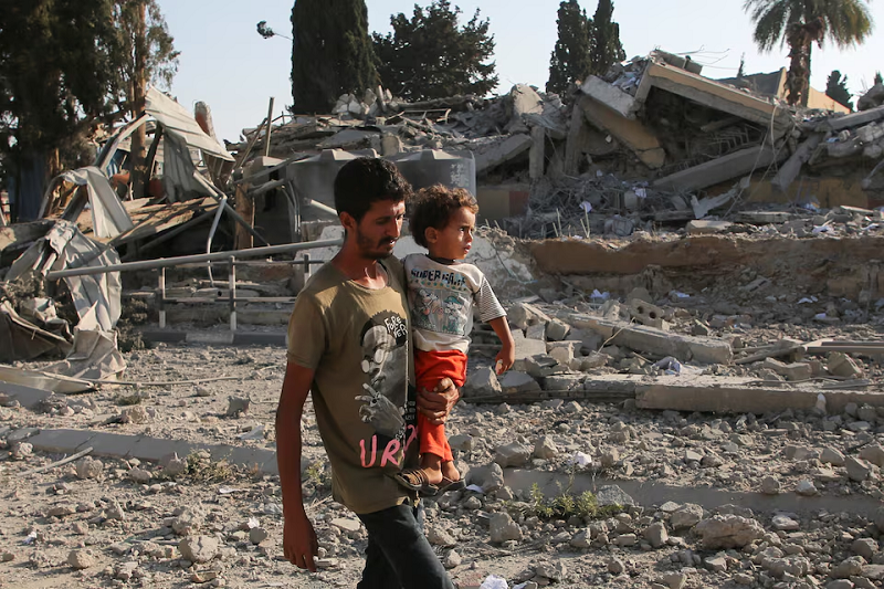 a palestinian man carries a child while walking near rubble in khan younis in the southern gaza strip june 27 2024 photo reuters