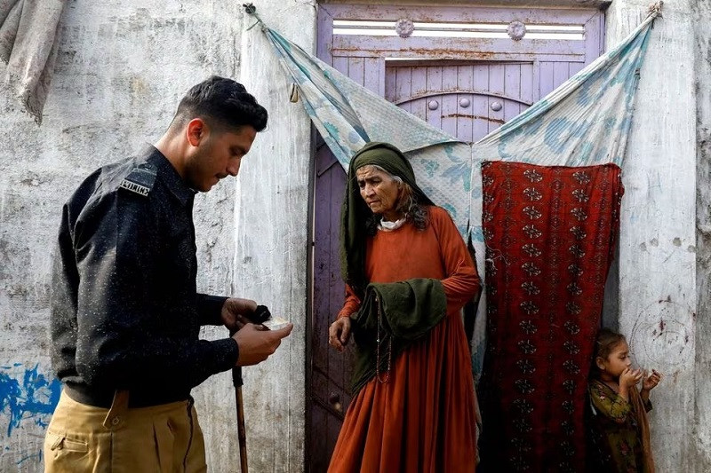 Edema Bibi, 66, an Afghan citizen, stands at the entrance of her house as a police officer checks her registration card in an Afghan Camp on the outskirts of Karachi, November 21, 2023. PHOTO; REUTERS