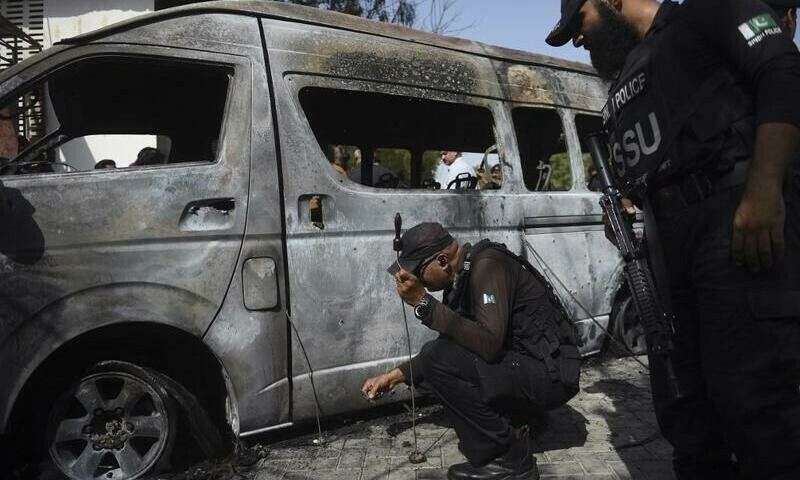 police inspect a site around damaged vehicles following a suicide bombing at a university in karachi on april 26 2022 photo afp