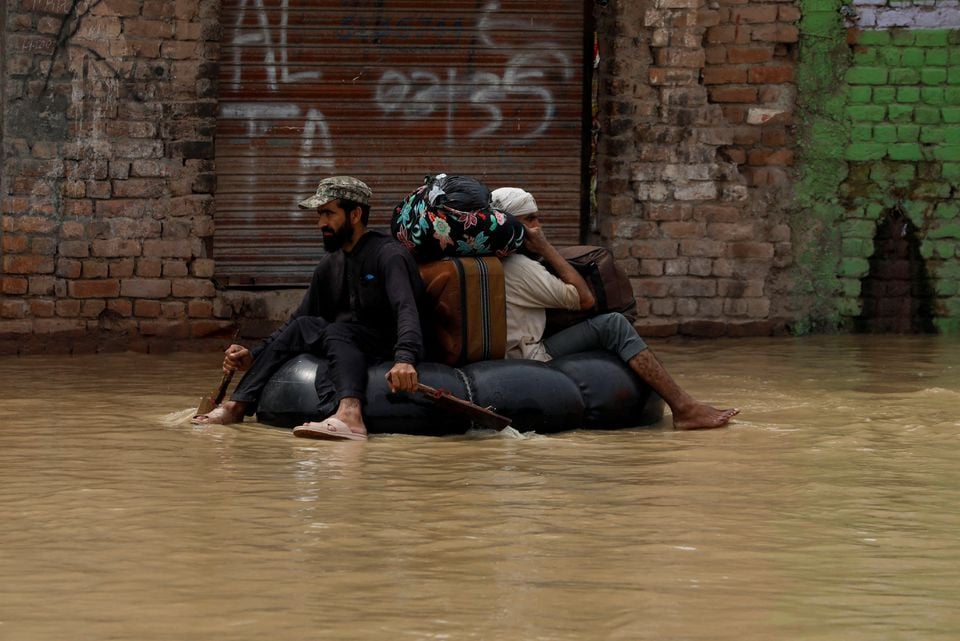 a volunteer paddles an inflatable tube as he evacuates a flood victim with his belongings following rains and floods during the monsoon season in charsadda pakistan august 27 2022 reuters