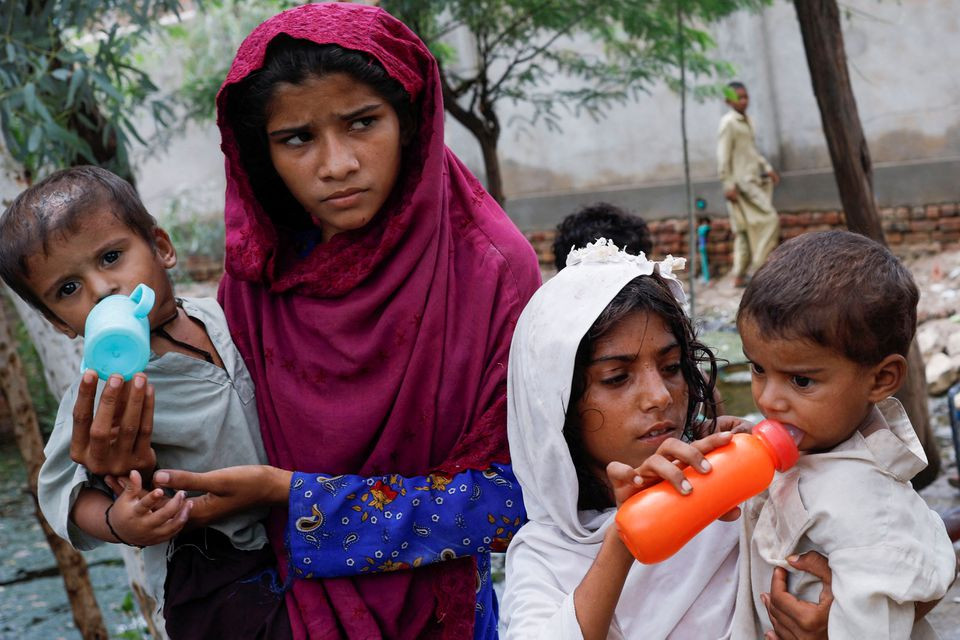 Girls, who along with their families are displaced by flooding, give water to their siblings, as they take refuge in a school, following rains and floods during the monsoon season, in Jacobabad, Pakistan August 30, 2022. REUTERS