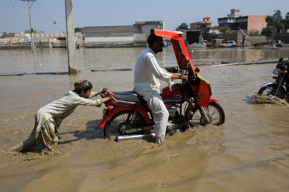 A boy pushes a motorbike after it stopped amid flood water, following rains and floods during the monsoon season in Nowshera, Pakistan August 30, 2022. REUTERS
