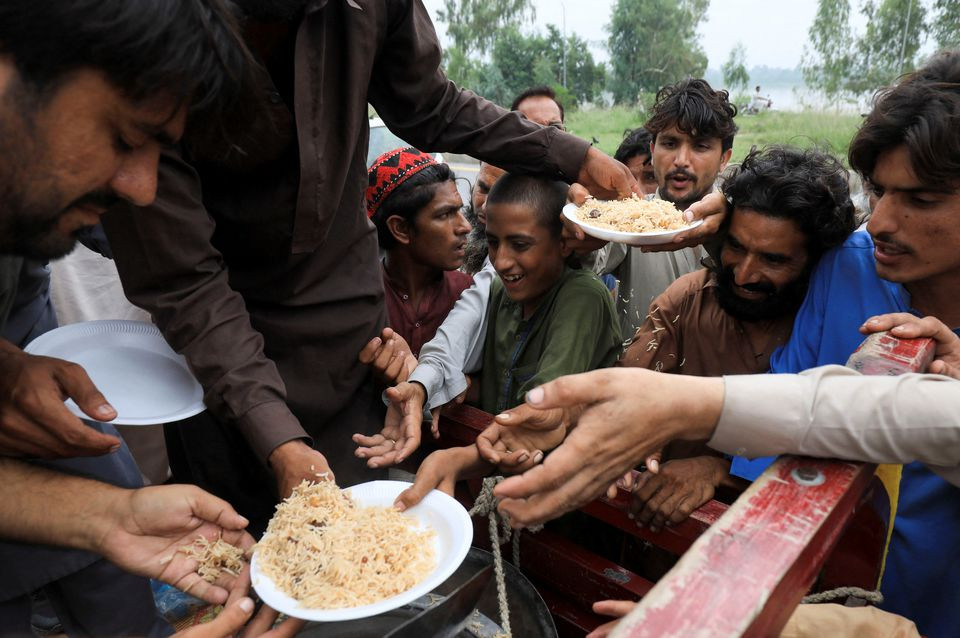 flood victims receive boiled rice from relief workers after taking refuge on a motorway following rains and floods during the monsoon season in charsadda pakistan august 27 2022 reuters