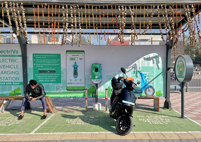 a man checks his mobile phone as he waits while recharging his ola electric scooter at an electric vehicle charging station in new delhi india february 12 2022 photo reuters