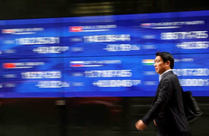 a passerby walks past an electric monitor displaying various countries stock price index outside a bank in tokyo japan photo reuters