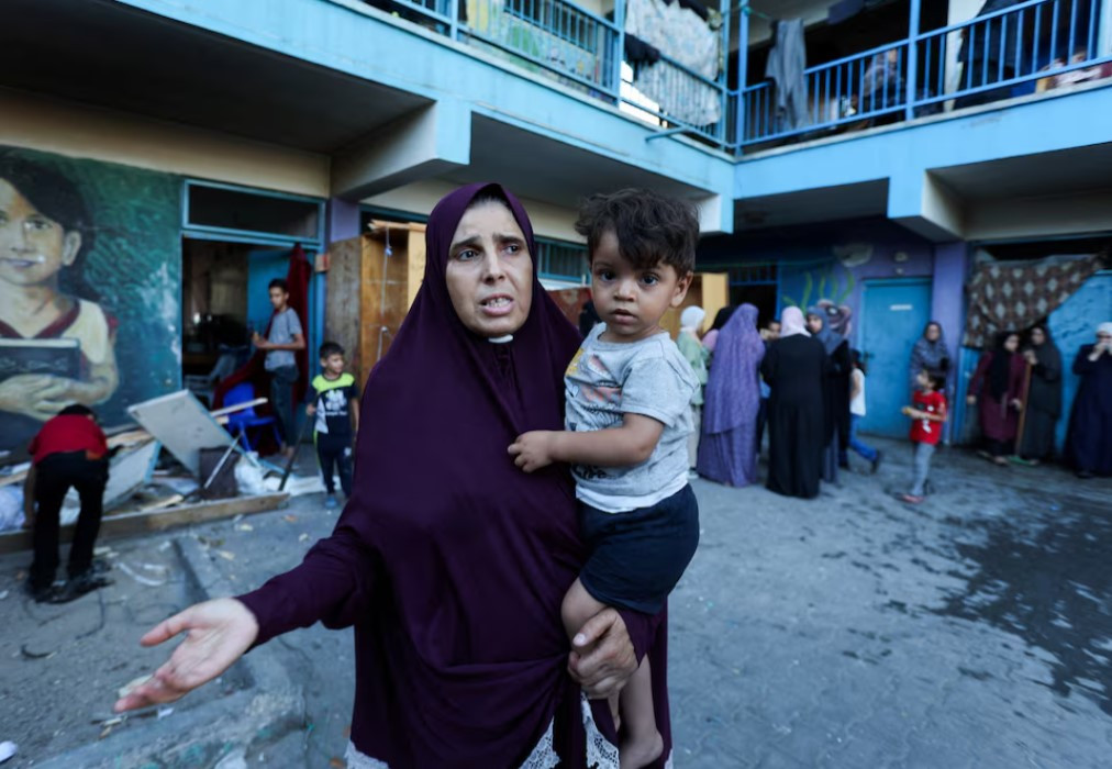 a palestinian woman carrying a child reacts after an israeli air strike on a un school sheltering displaced people amid the israel hamas conflict in nusairat in central gaza strip photo reuters