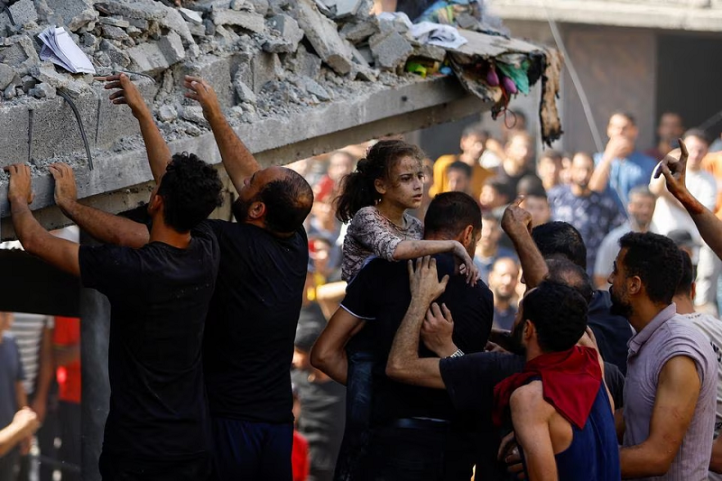 A Palestinian carries a child casualty at the site of an Israeli strike on a house, in Khan Younis, in the southern Gaza Strip, October 24. PHOTO: REUTERS