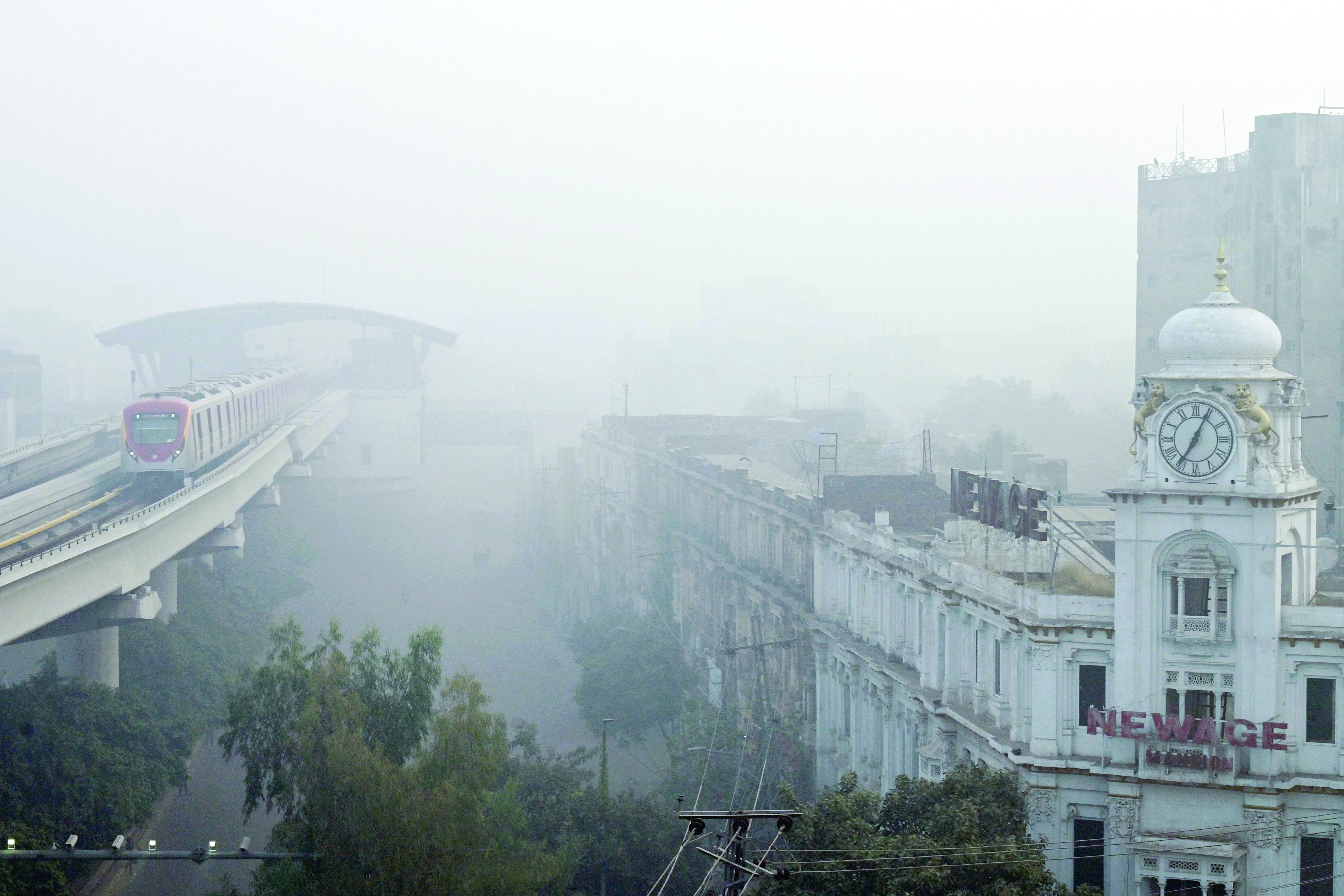 an orange line metro train runs on an elevated track amid smoggy conditions in lahore photo afp