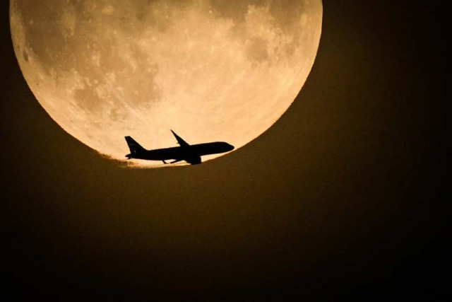 a british airways airbus a320 from belfast and preparing to land at heathrow flies past the full moon rising in the sky of london on august 30 2023 photo afp