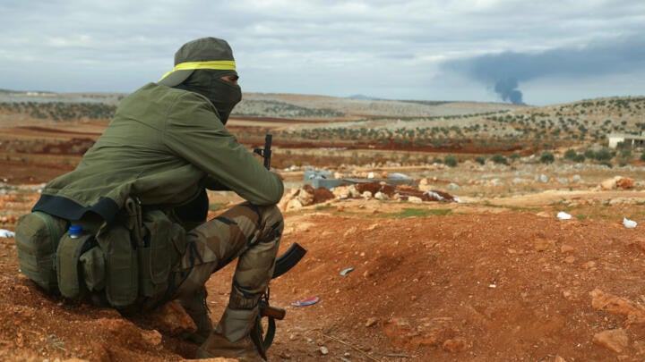 a fighter from hayat tahrir al sham hts mans a position in the eastern outskirts of atarib town in syria s aleppo province as smoke rises in the distance during clashes with the syrian army photo afp