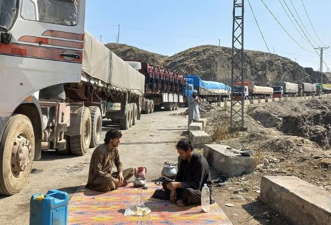 men sit near a queue of trucks loaded with supplies to leave for afghanistan after taliban authorities have closed the main border crossing in torkham pakistan february 21 2023 photo reuters