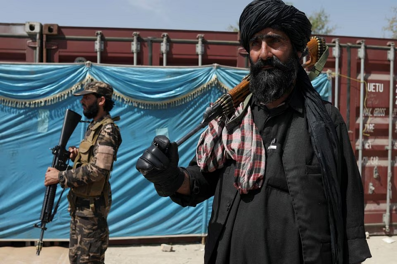 taliban fighters stand guard while people wait to receive sacks of rice as part of humanitarian aid sent by china at a distribution centre in kabul afghanistan april 7 2022 photo reuters