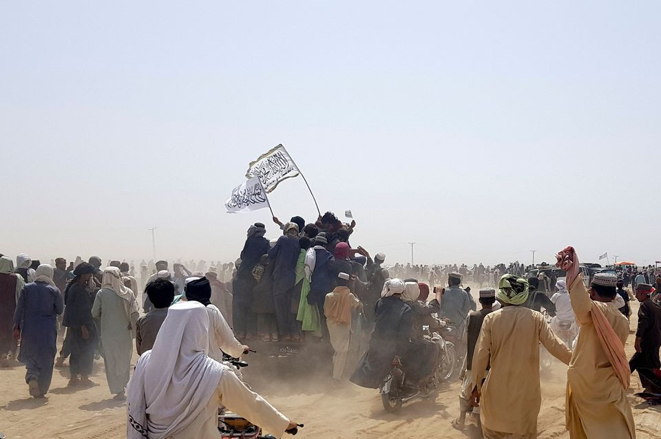 people standing on a vehicle hold taliban flags as people gather near the friendship gate crossing point in the pakistan afghanistan border town of chaman photo reuters