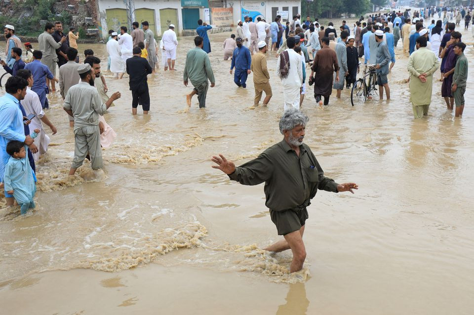 a man balances himself as he along with others walks on a flooded road following rains and floods during the monsoon season in charsadda pakistan august 27 2022 reuters