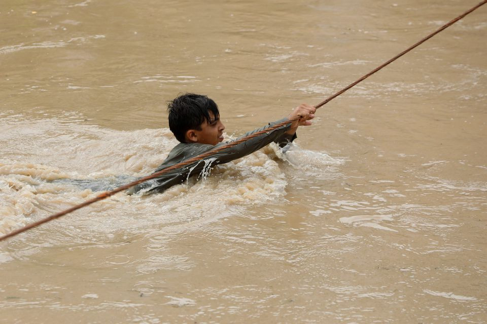 a boy crosses a flooded street with the help of a wire fastened on both ends following rains and floods during the monsoon season in charsadda pakistan august 27 2022 reuters