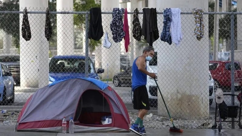 homeless man sweeps the sidewalk in front of his tent under a bridge where he is living in miami florida us photo ap