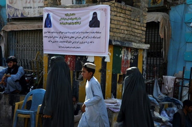 burqa clad women walk past a banner in kandahar telling them how to dress in public photo afp