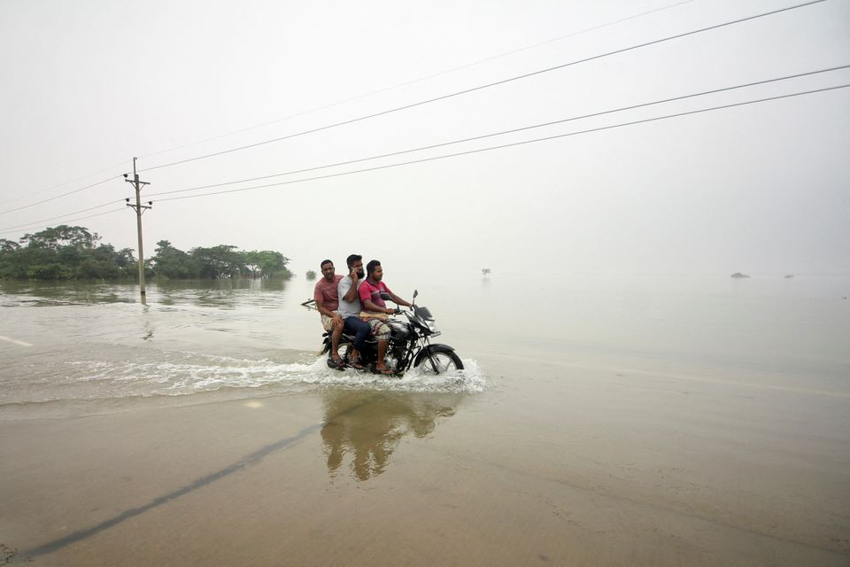 people ride on a bike on a submerged road during a widespread flood in the northeastern part of the country in sylhet bangladesh june 19 2022 reuters