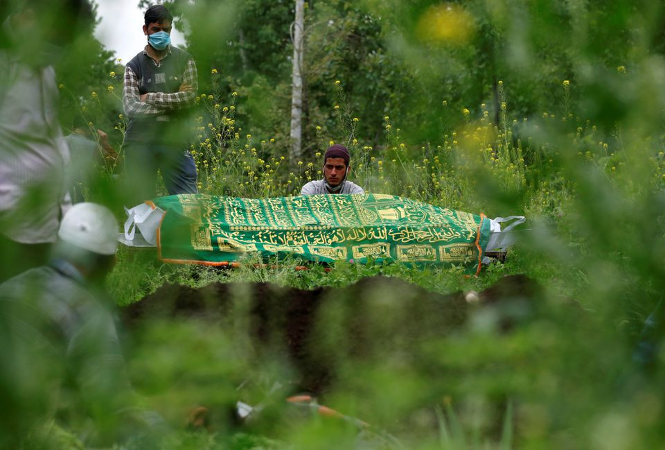 relatives are seen next to the body of a man who died due to the coronavirus disease covid 19 as they wait for a grave to be prepared for his burial at a graveyard on the outskirts of srinagar may 4 2021 reuters