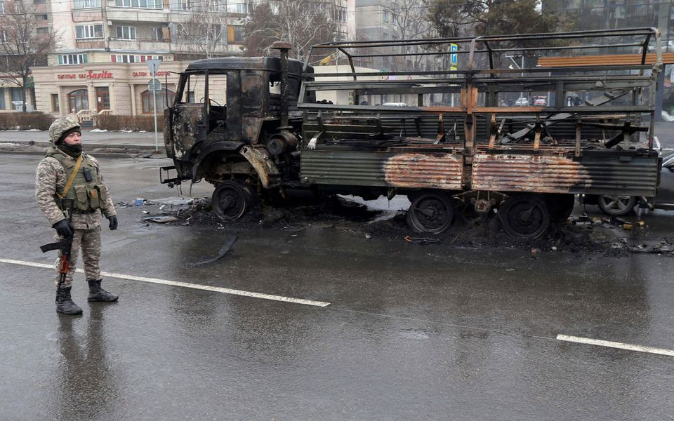 a kazakh law enforcement officer stands guard near a burnt truck while checking vehicles in a street following mass protests triggered by fuel price increase in almaty kazakhstan january 8 2022 reuters