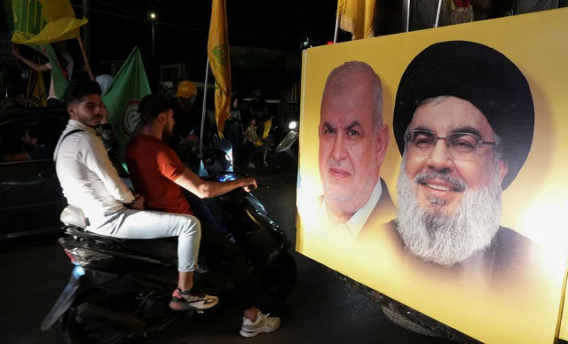 supporters carry hezbollah and amal movement flags as they ride in a convoy past a poster depicting hezbollah leader sayyed hassan nasrallah and head of hezbollah s parliamentary bloc mohamed raad as votes are being counted in lebanon s parliamentary election in nabatiyeh southern lebanon may 15 2022 reuters supporters carry hezbollah and amal movement flags as they ride in a convoy past a poster depicting hezbollah leader sayyed hassan nasrallah and head of hezbollah s parliamentary bloc mohamed raad as votes are being counted in lebanon s parliamentary election in nabatiyeh southern lebanon may 15 2022 reuters