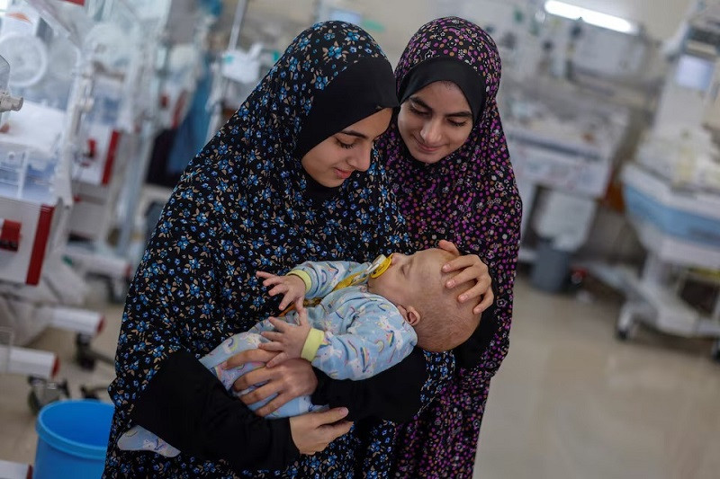 Alaa Abu Al-Roos and her sister look after Yehia Hamuda, a Palestinian infant, who was evacuated to south Gaza as a premature baby after Israeli forces raided Kamal Adwan hospital in northern Gaza Strip and is currently separated from his parents due to an Israeli checkpoint that separates north Gaza from the south, at Al-Emirati hospital, in Rafah in the southern Gaza Strip, April 24, 2024. PHOTO: REUTERS
