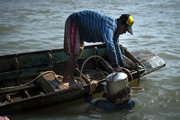 A boatman places a homemade metal scuba helmet on a diver. PHOTO: AFP