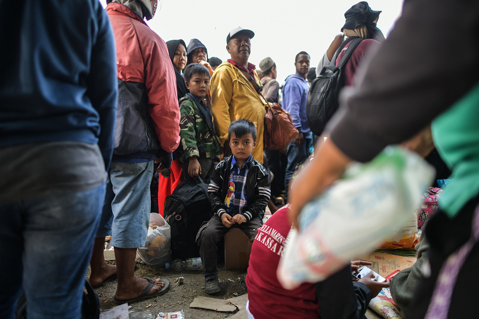 A boy sits as others queue behind a line before boarding military airplanes for evacuations at the Airport in Palu AFP