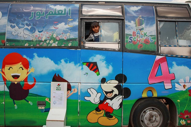 A displaced Syrian girl peaks out of the bus window (Photo: AFP)