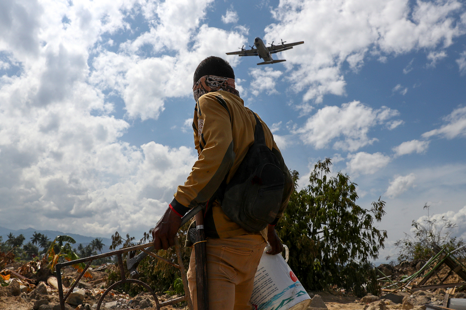 A villager carries his belongings as a military aircraft is about to land in an area after an earthquake hit Petobo neighbourhood in Palu, REUTERS