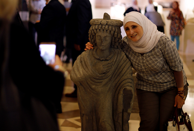 A woman poses for a picture with a restored sculpture, displayed in an exhibition, at the Opera house in Damascus, Syria REUTERS