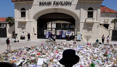 mourners stand near tributes piled together at the front of the bondi pavilion in memory of the victims of the bondi beach shooting in sydney on december 17 2025 photo afp