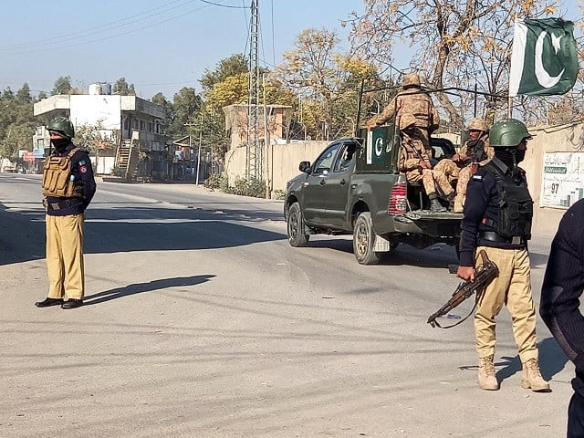 an army vehicle patrols past police officers who stand guard along a road near the cantonment area in bannu photo reuters