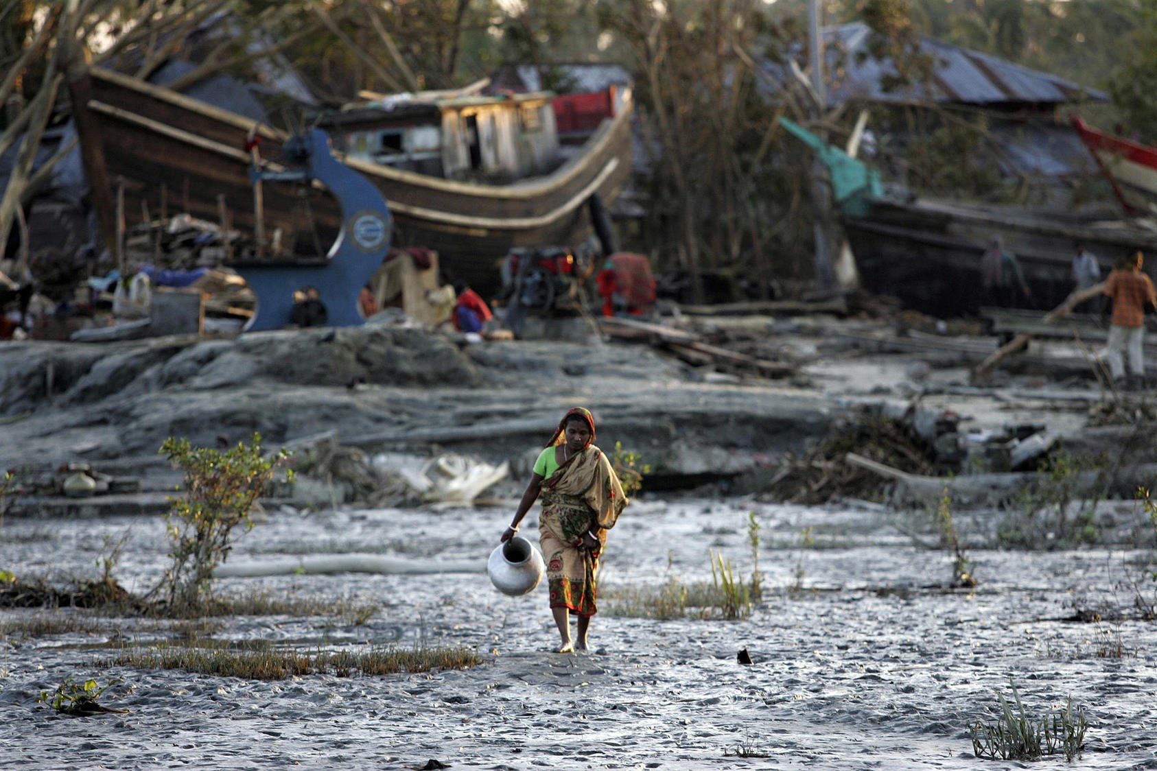 A woman carries water through the aftermath of a climate-induced disaster in a vulnerable coastal region of Bangladesh.