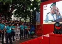 people watch muhammad yunus leader of bangladeshi interim government as he appears on a screen while reading the july declaration during celebrations marking the one year anniversary of student led protests that led to the ousting of bangladeshi then prime minister sheikh hasina at manik mia avenue outside the parliament building in dhaka bangladesh august 5 2025 photo reuters