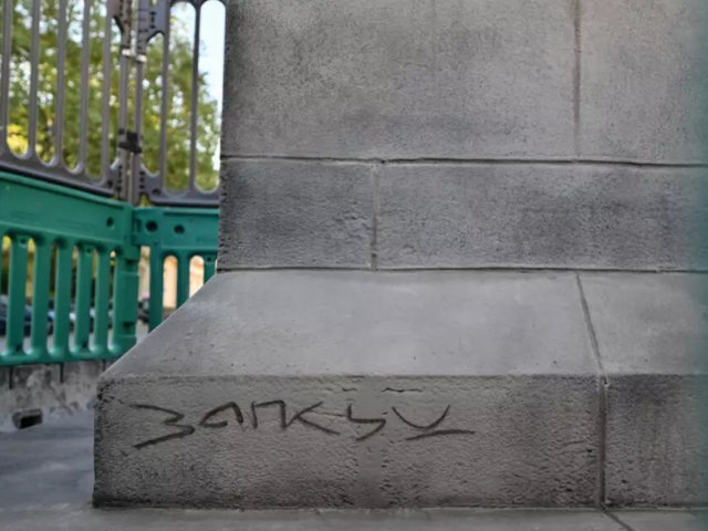 A signature bearing the likeness of British street artist Banksy is pictured etched onto the bottom of a new statue which suddenly appeared the day before, in Waterloo Place in central London early morning on April 30, 2026. A large statue has appeared on a plinth in central London with Banksy's name scrawled on the base, prompting speculation on April 30, 2026 that it may be the British street artist's latest work. The statue -- of a suited man marching, with one leg off the plinth, while carrying a flag that is covering his face -- reportedly first emerged just off Pall Mall on Wednesday. © Richard A. Brooks / AFP