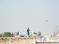 a boy flies a kite from the rooftop of his house in rawalpindi maneuvering it against the clear blue sky as the afternoon sun casts long shadows photo online