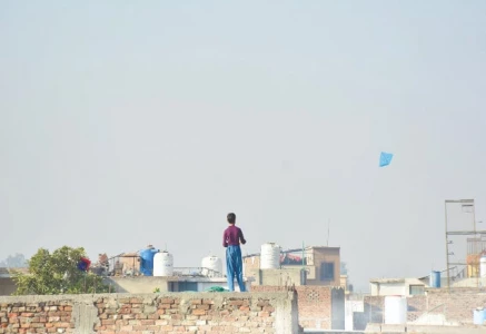 a boy flies a kite from the rooftop of his house in rawalpindi maneuvering it against the clear blue sky as the afternoon sun casts long shadows photo online