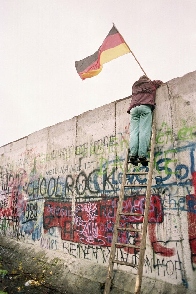 This file photo taken on November 11, 1989 shows a West Berliner preparing to hand over a FRG flag to East German Vopo policemen through a portion of the fallen Berlin Wall near the Brandenbourg Gate (Photo: AFP)