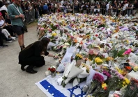 a woman keeps a candle next to flowers laid as a tribute at bondi beach to honour the victims of a mass shooting that targeted a hanukkah celebration at bondi beach on sunday in sydney australia december 16 2025 photo reuters