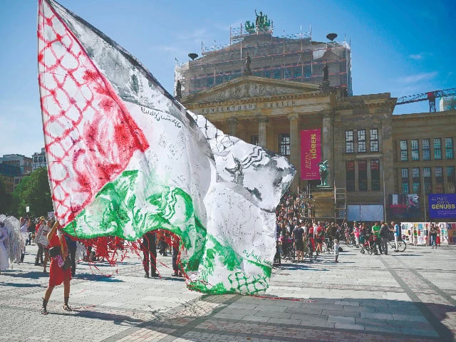 a demonstrator waves a giant palestinian flag as spectators gather for a classical concert at the gendarmenmarkt square outside the konzerthaus concert hall in berlin the concert was performed on world children s day on september 20 for the children of gaza photo afp