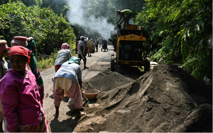 This photograph taken on March 26, 2026 shows construction workers operating a smoke-spewing tarmac mixer to build a road cutting through forest land, as part of the Great Nicobar Island Project. PHOTO: AFP