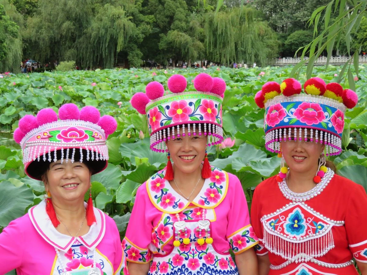 three women in vibrant traditional attire smile at a lotus pond in china showcasing cultural beauty photo pexels