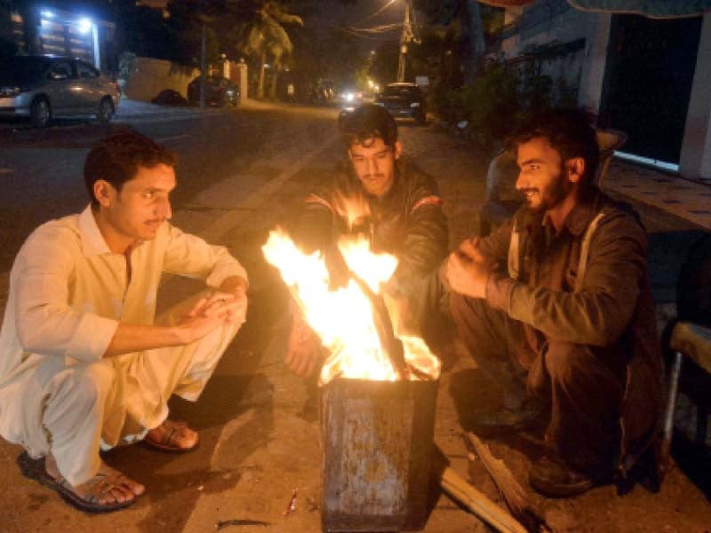 men sit around a fire on a cold night on a street in karachi photo express