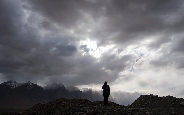 a man using a mobile phone before the Karakorum mountain range next to the China-Pakistan Friendship Highway near Tashkurgan in China's western Xinjiang province. PHOTO: AFP