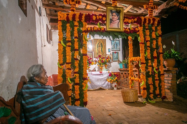 An elderly woman sits near offerings for the celebration of the Day of the Dead (Photo: AFP)