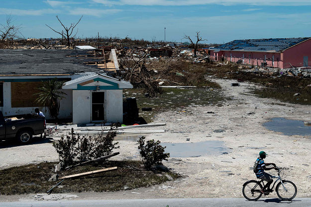 A man cycles passed damaged houses caused by Hurricane Dorian on September 5, 2019, in Marsh Harbour, Great Abaco Island in the Bahamas. PHOTO: AFP